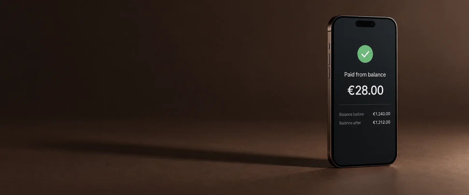 A phone standing on its own on a deep brown surface, its screen showing a green tick, the words paid from balance, twenty-eight euros, and two lines beneath reading balance before €1,240.00 and balance after €1,212.00.